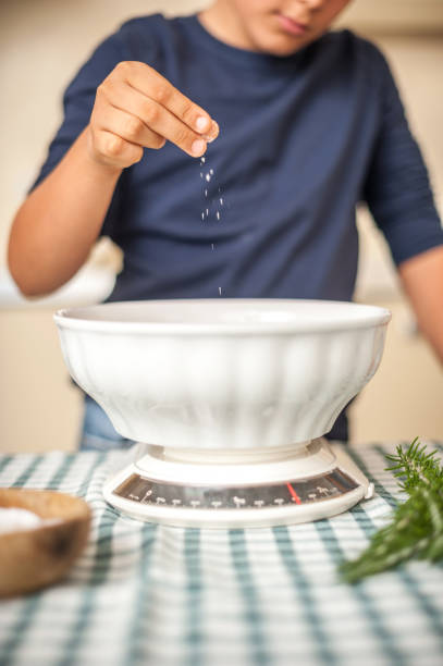 Boy Pouring Salt over Flour in Ceramic Bowl stock photo