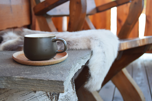 Dark green coffee cup outside on porch on mountain lodge with reindeer skins and chair.