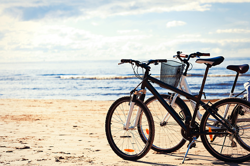 Two bicycles standing on the beach sand at the sea coastline with blue cloudy sky on background. Multicolored vibrant summertime horizontal outdoors image with retro filter and vintage tone