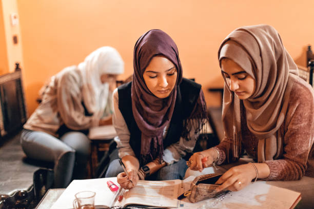 A beautiful Indonesian Muslim woman reading a book while sitting at a coffee shop table