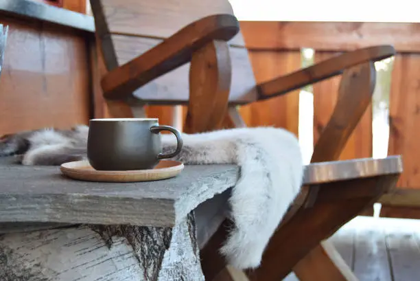 Dark green coffee cup outside on mountain lodge porch with reindeer skins and chair.