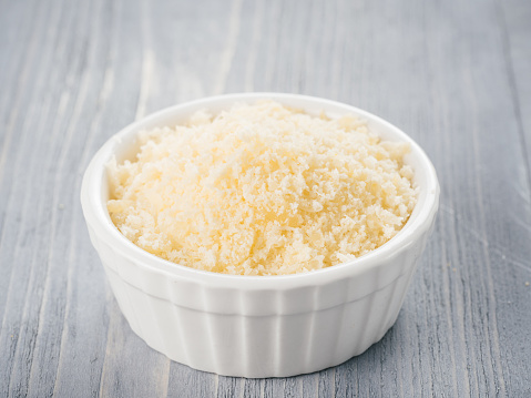 White ceramic bowl with freshly grated parmesan cheese on gray wooden background. Shredded parmesan on grey wooden table.