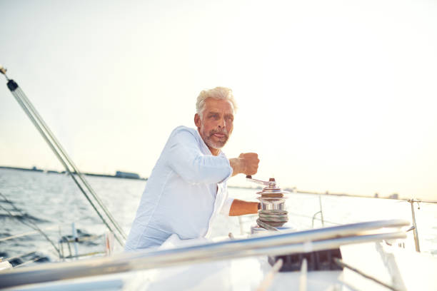 istock Mature man standing on his boat winding a winch 865768598