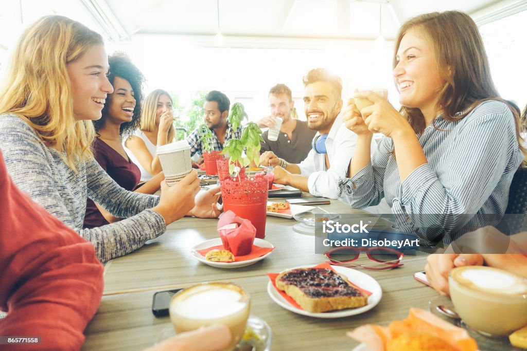 Happy friends having coffee break at bar cafe - Young hipster people enjoying breakfast - Friendship and good mood concept - Focus on right woman drinking cappuccino - Vsco filter Breakfast Stock Photo