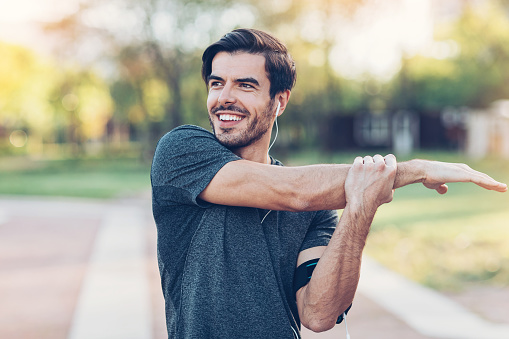 Smiling athlete making stretch exercises in the park