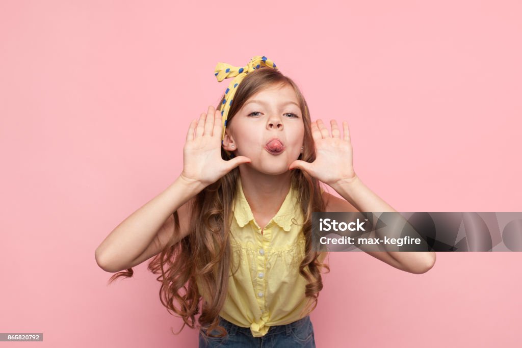 Girl showing tongue at camera Little charming model looking at camera and showing tongue on pink background. Child Stock Photo