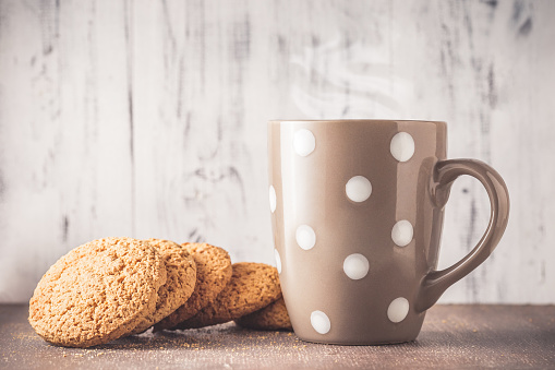 Oat cookies and polka dot mug with hot drink over wooden background