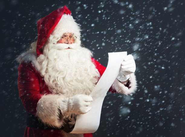 Santa Claus reading from a long list, over a dark background with snow stock photo