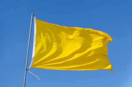 Yellow flag attached to a flagpole waving on the sky