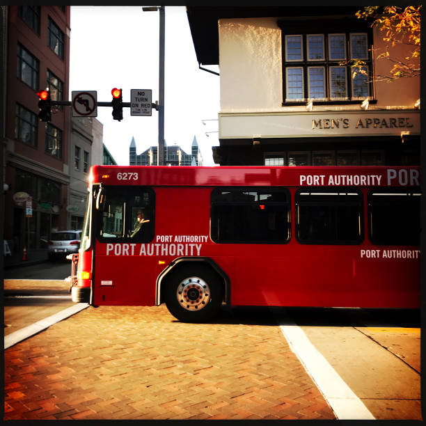 Pittsburgh, USA     October 22, 2017     Red Port Authority bus moving along Fifth Avenue in downtown Pittsburgh during early morning sun. Driver can be seen in window.  iPhone