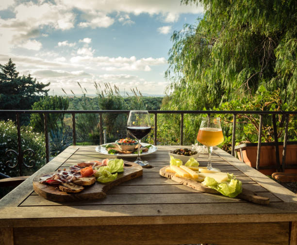 Appetizer for two on a terrace and landscape view. Beer glass, wine glass, cheese, olives, bread, lettuce and ham on a wooden table italian cheese stock pictures, royalty-free photos & images