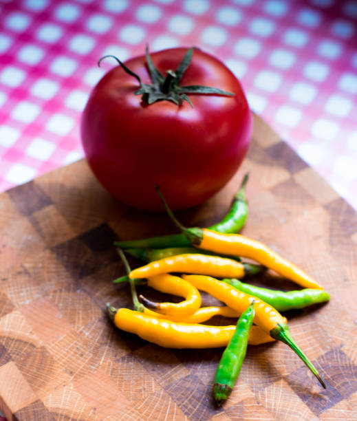Chilli peppers and a red tomato on a cutting board