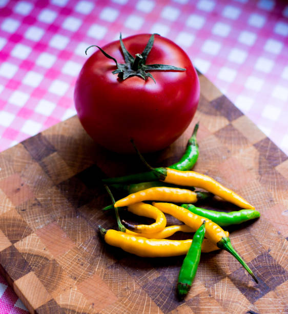 istock Chilli peppers and a red tomato on a cutting board 865857792