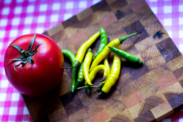 Chilli peppers and a red tomato on a cutting board