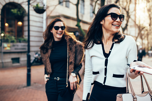 Two women on city street having fun. Female friends on walking down the road and smiling outdoors.