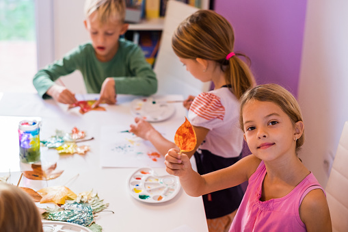 Children painting while little girl showing colored leaf