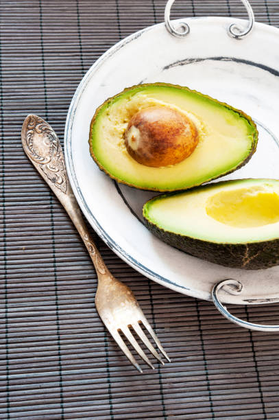 avocado dimezzato su piatto vintage con forchetta. - avocado cross section vegetable seed foto e immagini stock