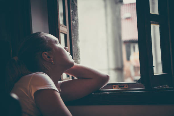 Lonely pensive women with thoughtful expression lost in thoughts thinking and looking in opened  window in vintage style with dramatic mood