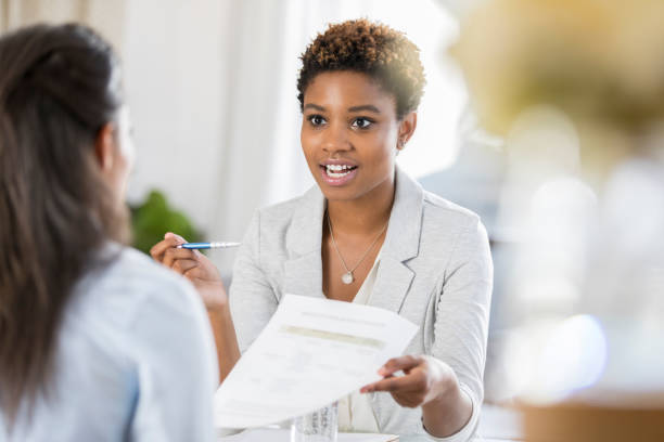 Businesswomen meet to discuss document Young businesswoman has a serious expression on her face while discussing a document with a female colleague. handing out stock pictures, royalty-free photos & images