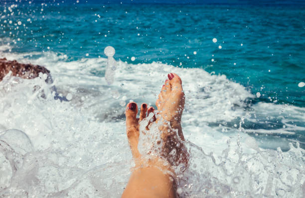 Female legs covered with a splash and foam of a sea wave
