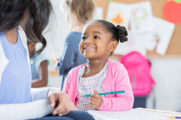 istock Adorable toddler grins while drawing in her classroom 865903206