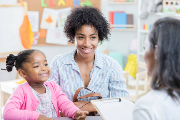 African American mom talks with teacher during conference Young African American mom has a conference with her young daughter's preschool teacher. The little girl is sitting next to her mother. preschool building photos stock pictures, royalty-free photos & images