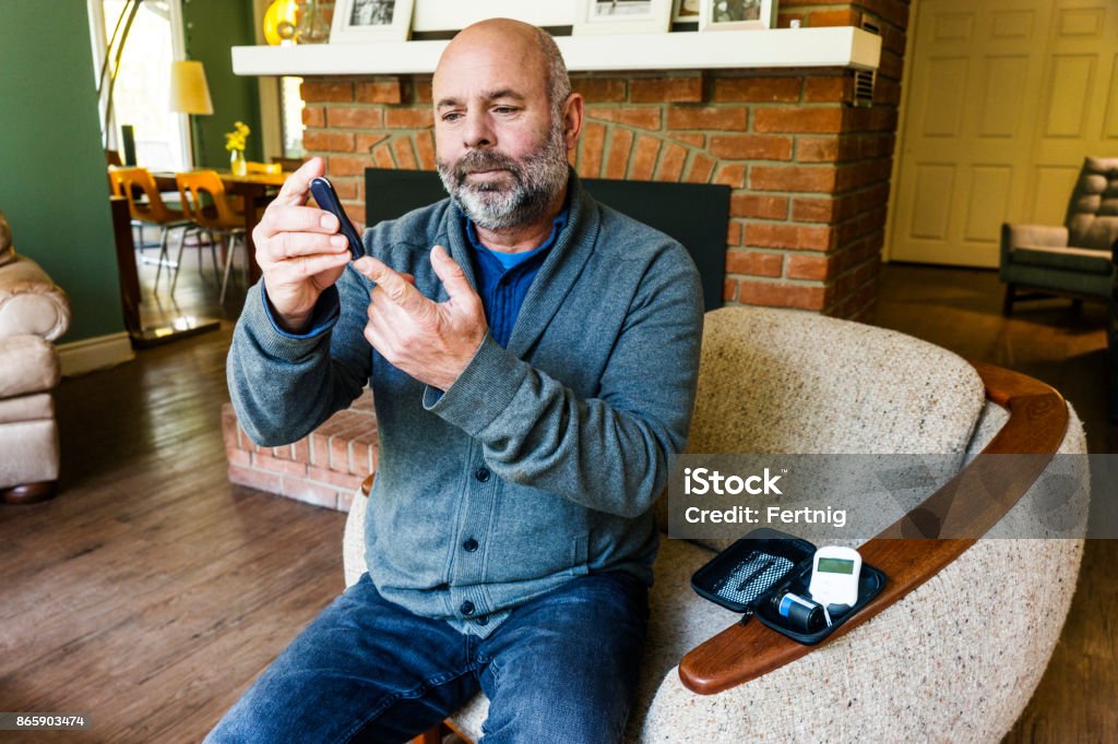 Mature diabetic patient taking a blood test A mature man in his fifties at home testing his blood sugar levels. Diabetes Stock Photo