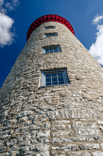 Skyward view of an 1800's lighthouse stone tower reaching into a blue sky with puffy clouds.