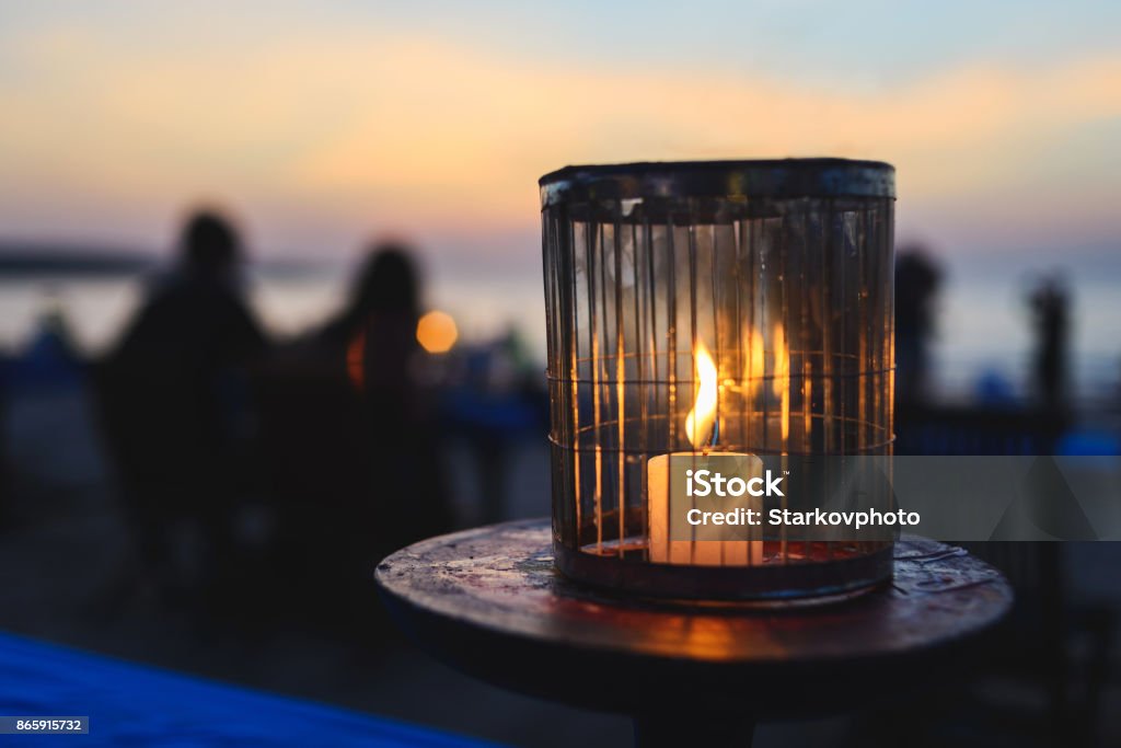 Romantisches Abendessen in einem Café am Meer bei Sonnenuntergang. Eine Kerze brennt auf dem Tisch für die Gäste in einem Café. - Lizenzfrei Im Freien Stock-Foto