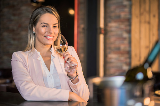 Beautiful young woman enjoying white wine in the bar
