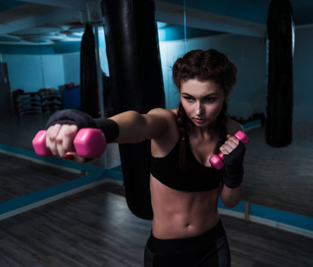 Young fighter boxer girl with hand bandage in training with dumb Strong young fighter boxer girl with hand bandage in training with pink dumbbells. Woman power and beauty boxercise stock pictures, royalty-free photos & images