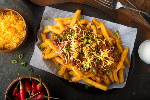 Delicious homemade spicy chili fries with green onion and cheddar cheese.
