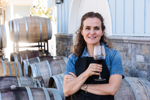 mature caucasian woman posing holding a glass of wine at her winery