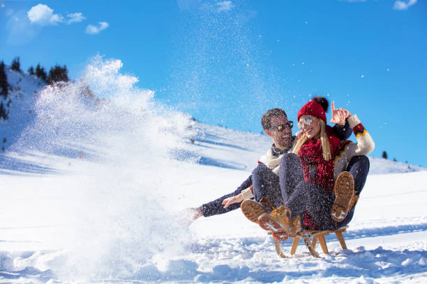 Young Couple Sledding And Enjoying On Sunny Winter Day.