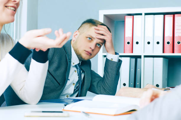 istock Pensive young handsome man looking on his colleague while sitting at the office table on business meeting. 865955946