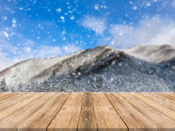 istock Wooden board empty table top on of blurred snowfall background. Perspective brown wood table over blur winter blue landscape background - used mock up for montage products display or design background 865965556
