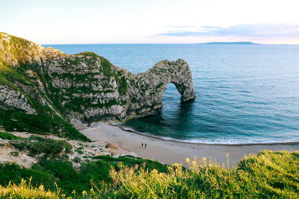 vue depuis la colline plus personnes marcher sur une plage de la mer et le durdle door, le uk - horizon over water england uk summer photos et images de collection