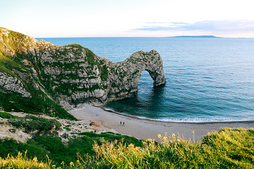 View from the hill over people walking on a beach by the sea and Durdle Door, a natural limestone arch on Dorset's Jurassic Coastline, UK