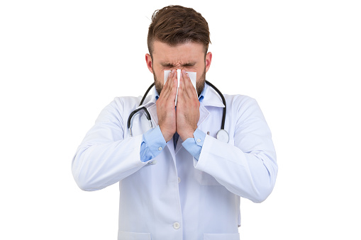 Young Doctor sneezing isolated against white background.
