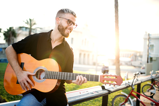 Smiling musician playing guitar on sunset