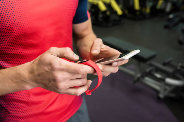 Sportsman using Fitness Device in Gym Closeup of strong male hands setting up fitness bracelet checking data on smartphone while working out in modern gym, copy space fitness tracker stock pictures, royalty-free photos & images
