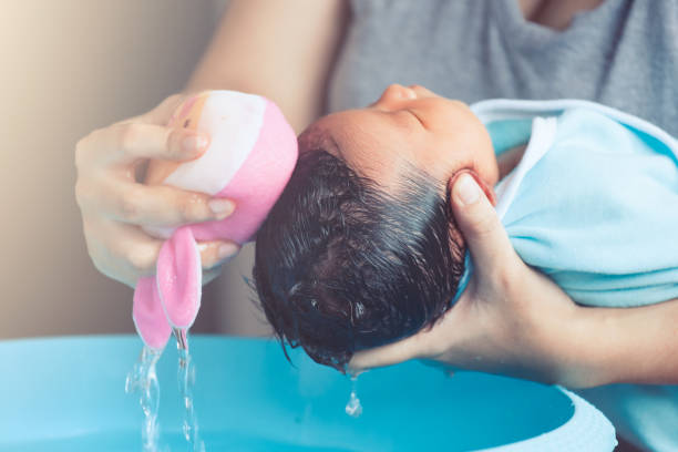Cute asian newborn baby girl take a bath. Mom cleaning her baby hair with sponge stock photo