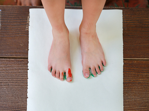 Child painted foot with color green-orange on the paper.