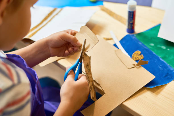 petit garçon coupe papier en classe de bateaux - fait maison photos et images de collection