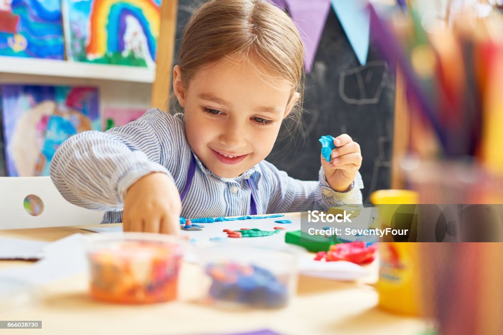 Happy Little Girl in Development School Portrait of smiling little girl working with plasticine in art and craft class of development school Child Stock Photo