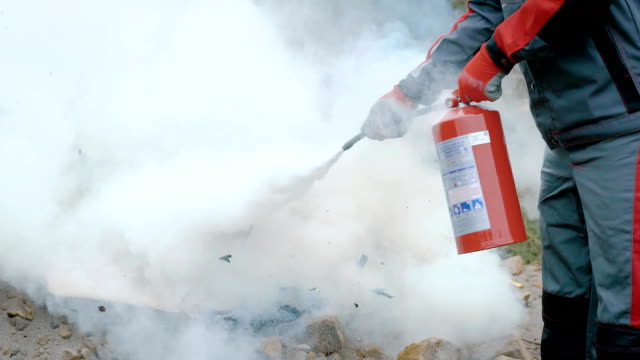 A man holds a fire extinguisher in his hands and extinguishes the fire box with a foam, the fire is stopped with a safety device