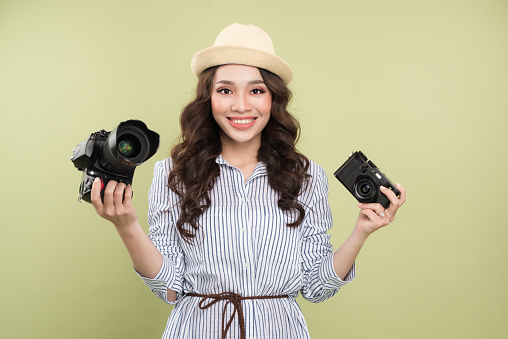 Young asian woman comparing professional and compact cameras on green background
