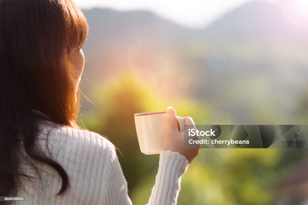 Coffee time on the mountain, rear view. Woman drinking hot coffee outdoor enjoying sunrise and landscape during vacation on the mountain with rim light effect,holiday concept. Coffee - Drink Stock Photo