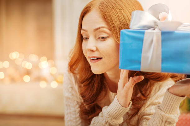 Curious redhead lady guessing what she got for christmas What is inside. Excited woman cannot wait to open her Christmas present and trying to guess what she got on Christmas morning. hair covering eyes stock pictures, royalty-free photos & images