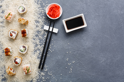 Japanese restaurant, sushi roll, maki platter. Set for one person with black chopsticks, ginger, soy on rustic grey and white rice background. Top view, copy space